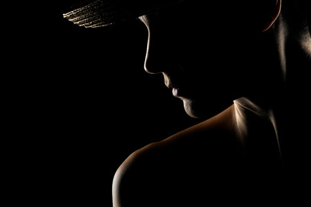 Sensual portrait silhouette of beautiful woman with a hat in backlight on a black studio backgroundの写真素材