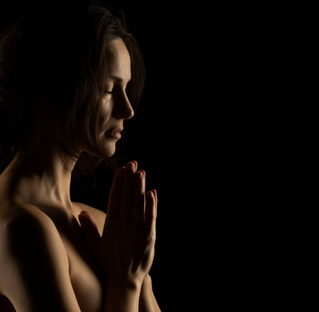 Silhouette of young praying woman on black studio backgroundの写真素材