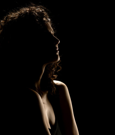 Sensual portrait silhouette of beautiful curly woman in backlight on a black studio backgroundの写真素材