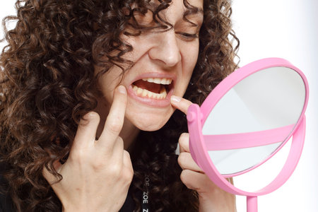 young woman looking her teeth on the mirror on a white studio backgroundの写真素材