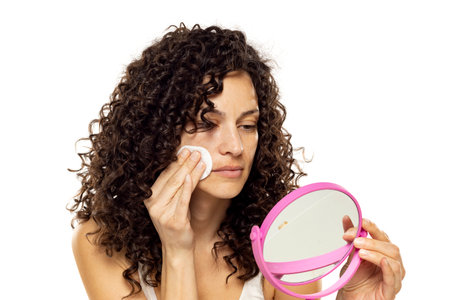 Skincare Concept. Attractive Curly Woman Removing Makeup Using Cotton Pad Cleansing Face Skin Over Gray Studio Background.の写真素材