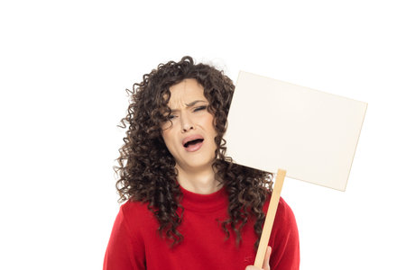 Young curly unhappy woman holding blank sign on white studio background.の写真素材