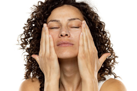Portrait of an attractive young woman apply a beauty product on her face against a white studio background.の写真素材