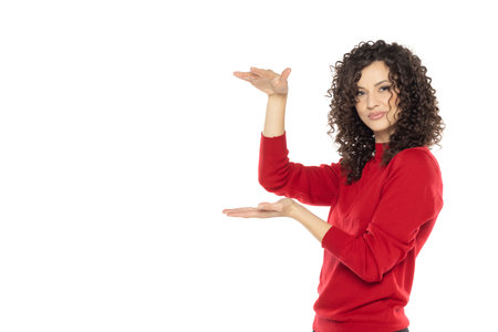 portrait of a young happy curly woman on a white studio background, advertise some product.の写真素材