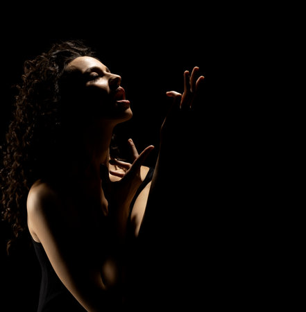 Sensual portrait silhouette of beautiful curly woman with outstretched hand sings in backlight on a black studio backgroundの写真素材