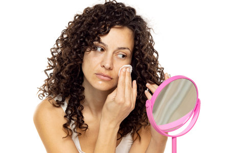 Skincare Concept. Attractive Curly Woman Removing Makeup Using Cotton Pad Cleansing Face Skin Over White Studio Background.の写真素材