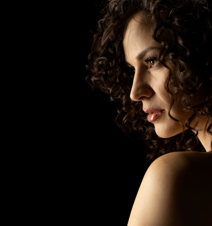 Sensual portrait of beautiful curly serious curly woman a black studio backgroundの写真素材