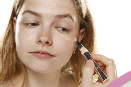 young blond woman apply concealer under the eye on a white studio backgroundの写真素材
