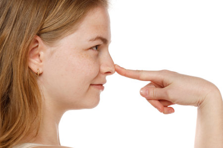 Profile of young woman touching her nose on a white studio backgroundの写真素材