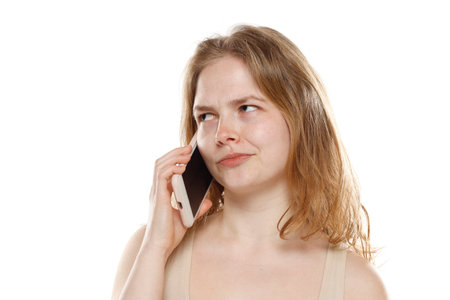 Portrait of young beautiful nervous blonde woman with no makeup talk on the mobile phone on white studio backgroundの写真素材