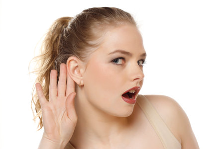 Young caucasian blonde woman listening to something by putting hand on the ear on a white studio backgroundの写真素材