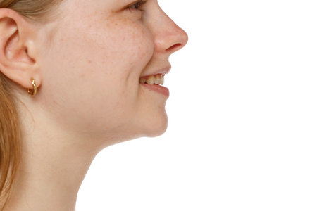 Closeup profile of a young woman's face, smile, mouth, nose and cheek on a white studio background