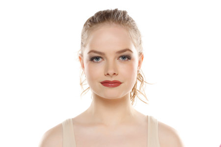 Portrait of young beautifu smiling blonde woman with makeup and tied hair on white studio backgroundの写真素材