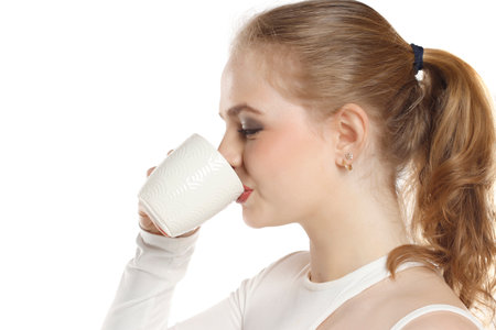 Beautiful young blond woman drinking coffee on white studio backgroundの写真素材