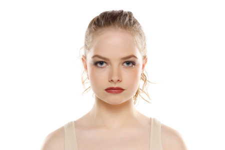 Portrait of young beautifu serious blonde woman with makeup and tied hair on white studio backgroundの写真素材