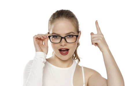 Portrait of beautiful positive blonde woman wearing glasses and pointing up on a white backgroundの写真素材