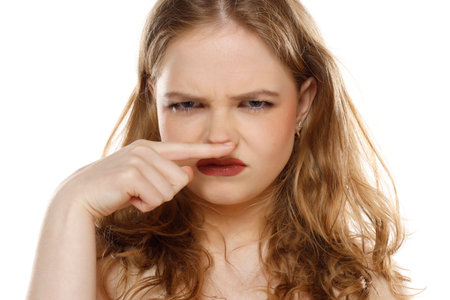 Bad smell stinks. Young beautiful blonde woman finger under with disgust on a white studio backgroundの写真素材