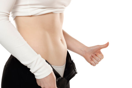 Fit woman showing flat belly and showing thumbs up on a white studio background. Closeup.の写真素材