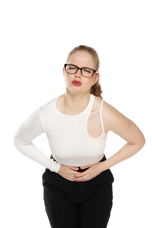 Woman having stomach ache, bending and holding hands on belly, discomfort from menstrual cramps on a white studio backgroundの写真素材