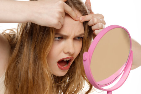 Nervous beautiful blonde woman squeeze pimples on her face on a white studio backgroundの写真素材