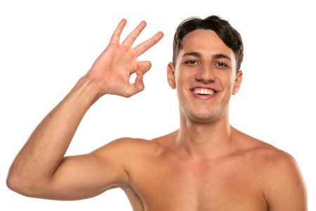 Closeup portrait of happy shirtless man 20s  looking at camera and showing delicious gesture isolated over white studio backgroundの写真素材