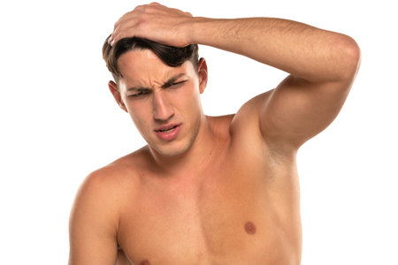 Closeup portrait of shirtless 20s man with headache isolated over white studio backgroundの写真素材
