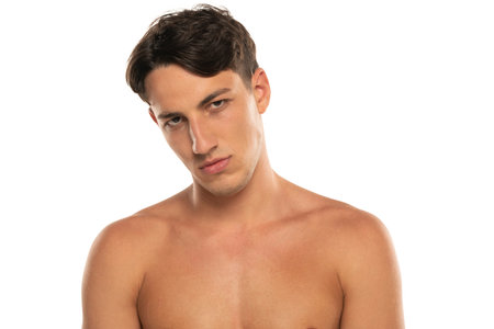 Closeup portrait of sullen half naked man 20s  looking at camera isolated over white studio backgroundの写真素材
