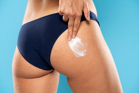 Cropped shot of slim young woman in underwear applying body cream on her bottom on a blue studio backgroundの写真素材