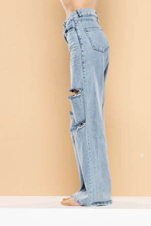 legs of a woman in ripped jeans on a beige studio background. Side, profile view.の写真素材