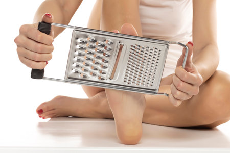 a woman scrapes her feet with a kitchen grater on a white studio backgroundの写真素材