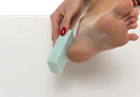 woman file her feet with a pumice stone on white studio backgroundの写真素材