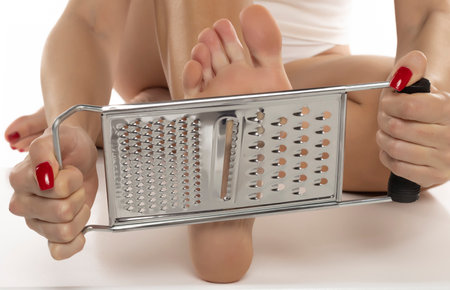 a woman scrapes her feet with a kitchen grater on a white studio backgroundの写真素材