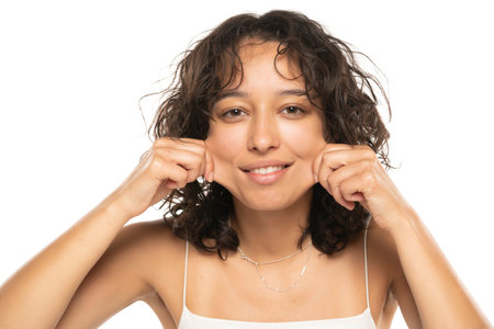 Portrait of young etnic woman, pulling her cheek skin on white studio backgroundの写真素材