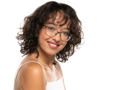 Young dark skinned smiling woman with makeup, glasses  and wavy hair posing on a white studio backgroundの写真素材