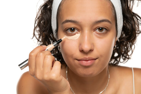 Young etnic woman applyes concealer under her eyes on white studio backgroundの写真素材