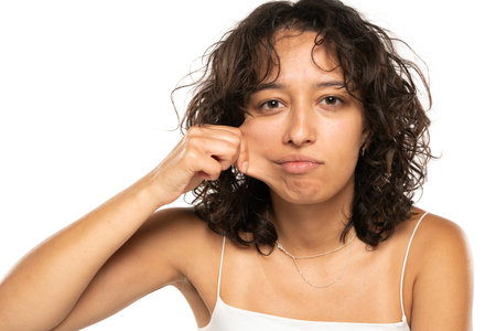 Portrait of young etnic woman, pulling her cheek skin on white studio backgroundの写真素材
