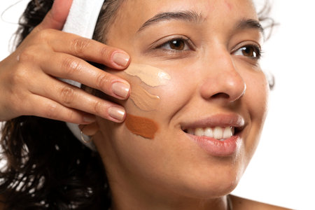 Face of dark skinned woman with tree different tones of liquid foundation on a white studio backgroundの写真素材