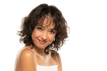 Young dark skinned smiling woman with makeup and wavy hair posing on a white studio backgroundの写真素材