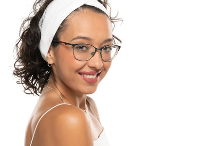 Young dark skinned smiling woman with makeup, headband and glasses posing on a white studio backgroundの写真素材