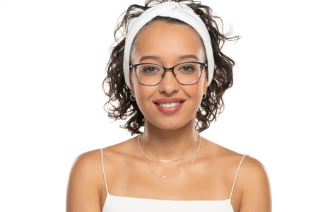Young dark skinned smiling woman with makeup, headband and glasses posing on a white studio backgroundの写真素材