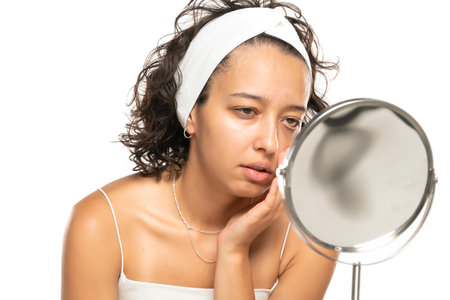 disappointed etnic woman without makeup looking herself in the mirror on a white studio backgroundの写真素材