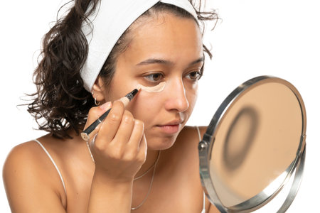 Young etnic woman applyes concealer under her eyes on white studio backgroundの写真素材