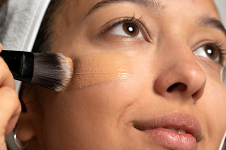 Young etnic woman applyes liquid founation on her face with makeup brush on white studio  backgroundの写真素材