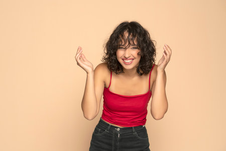 Young exotic happy brunette woman in red sleeveless shirt and jeans posing  on a beige studio backgroundの写真素材