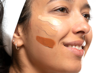 Face of dark skinned woman with tree different tones of liquid foundation on a white studio backgroundの写真素材