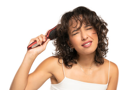 Young dark skinned woman with makeup has a problem with combing her wavy hair on a white studio backgroundの写真素材