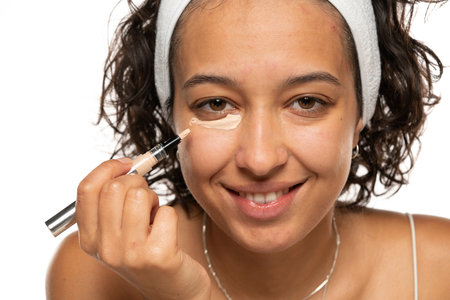 Young etnic woman applyes concealer under her eyes on white studio backgroundの写真素材