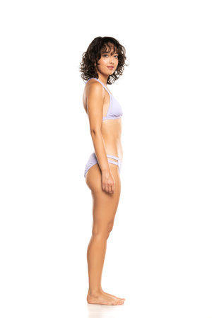 Young smiling exotic brunette woman in lilac bikini swimsuit posing on a white studio background. Side, profile view.の写真素材