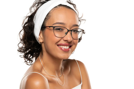 Young dark skinned smiling woman with makeup, headband and glasses posing on a white studio backgroundの写真素材
