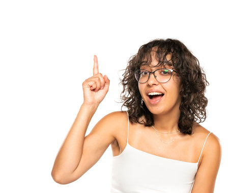 Young dark skinned happy woman with glasses and wavy hair has an idea on a white studio backgroundの写真素材